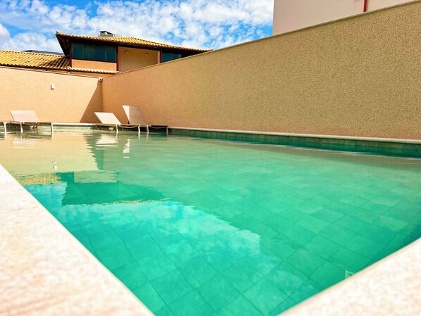 A swimming pool with clear water, surrounded by beige walls and a building with a tiled roof.