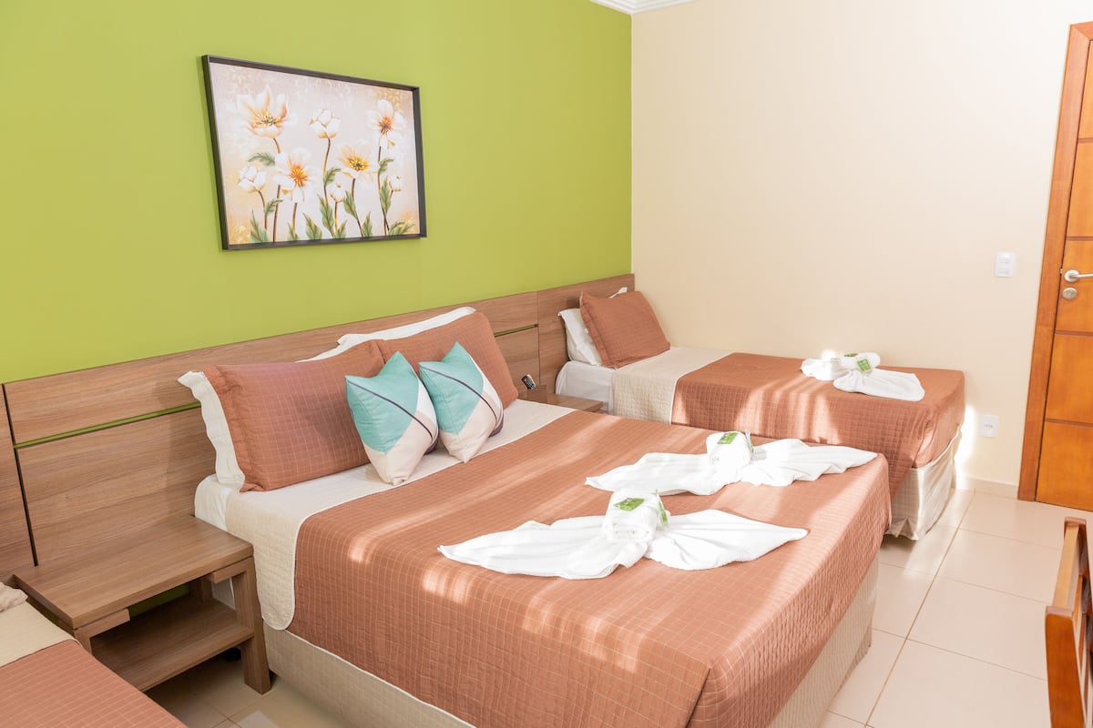 Une chambre d’hôtel avec deux lits, un mur vert et un tableau floral encadré.