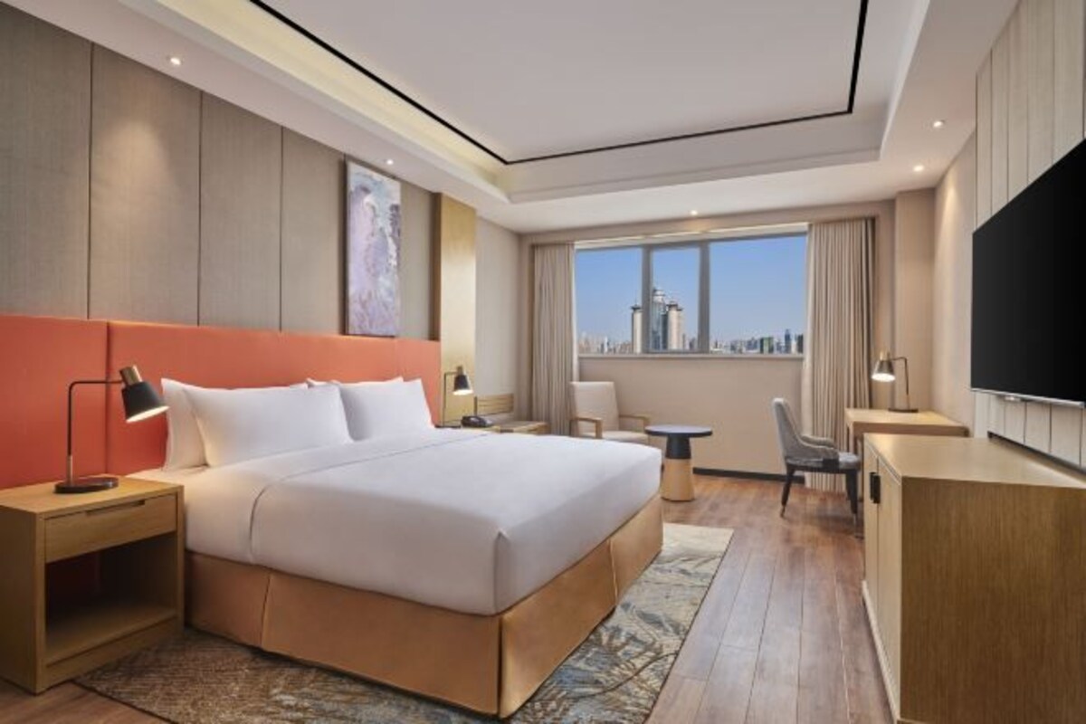 Une chambre d’hôtel moderne dotée d’un grand lit, d’un bureau, d’une télévision et offrant une vue sur le panorama urbain.
