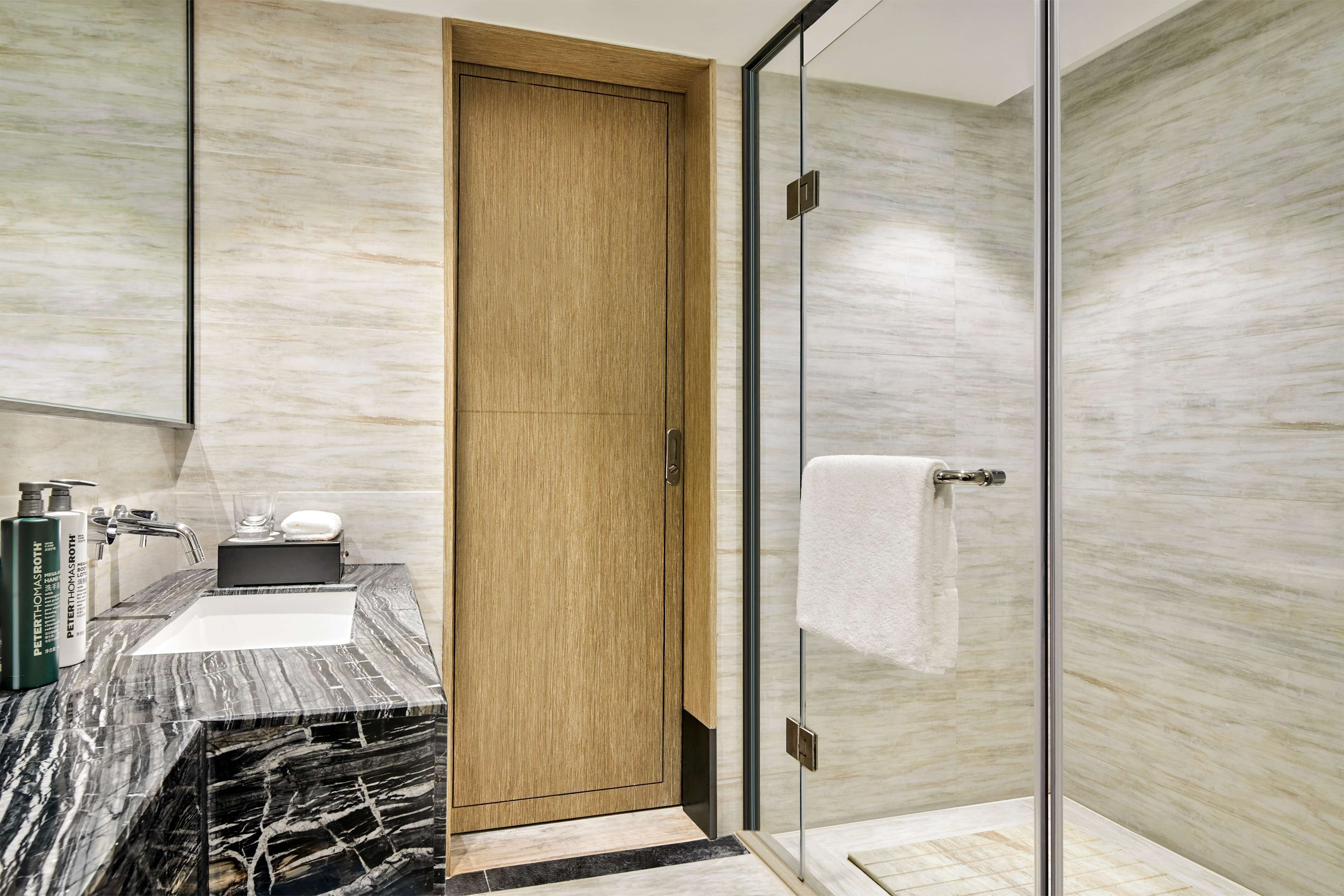 A modern bathroom with a wooden door, a glass shower enclosure, and a marble sink.