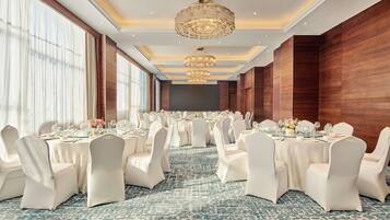A banquet hall with round tables, white chairs, and chandeliers.