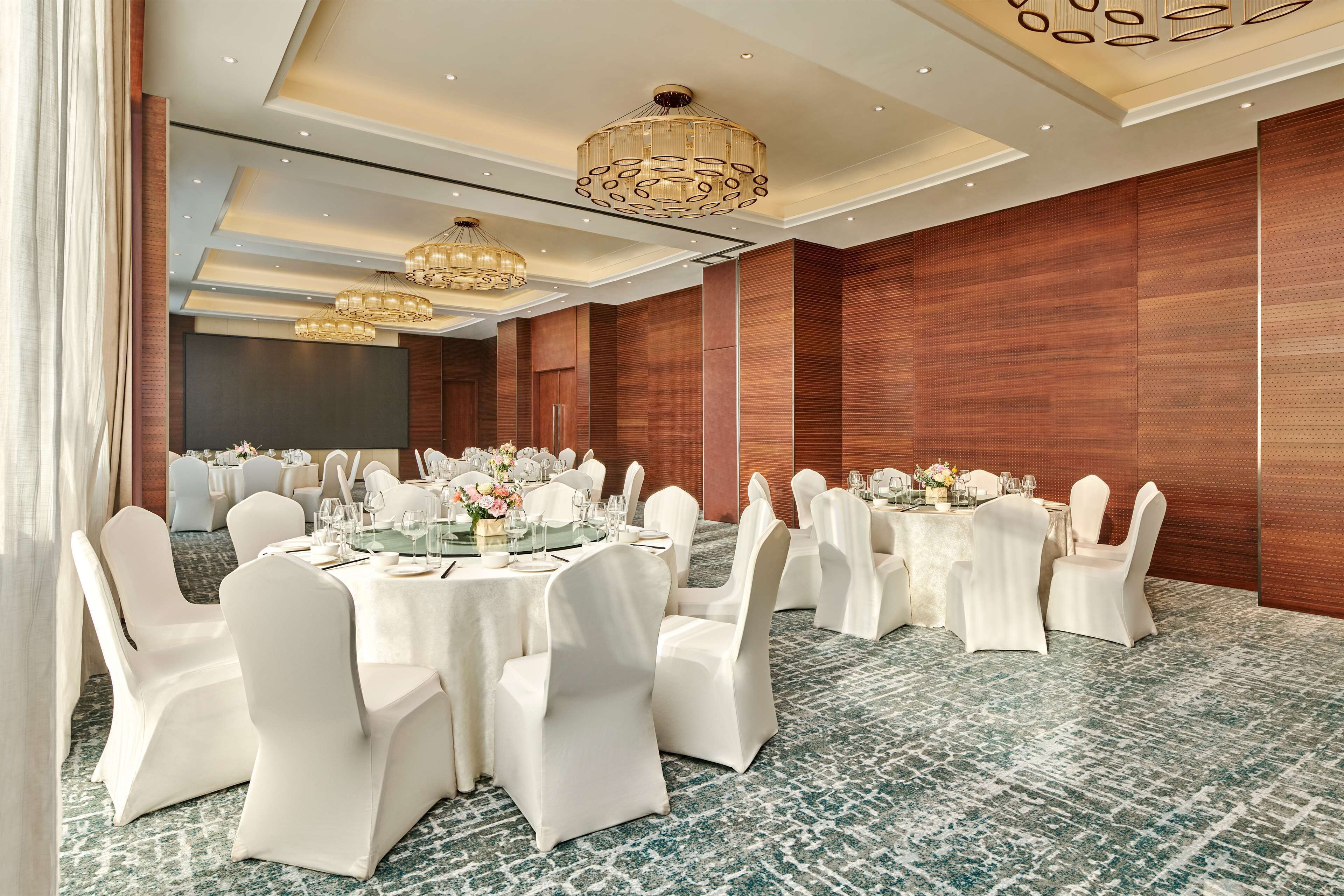 Une salle de banquet avec des tables rondes, des chaises blanches et des lustres.