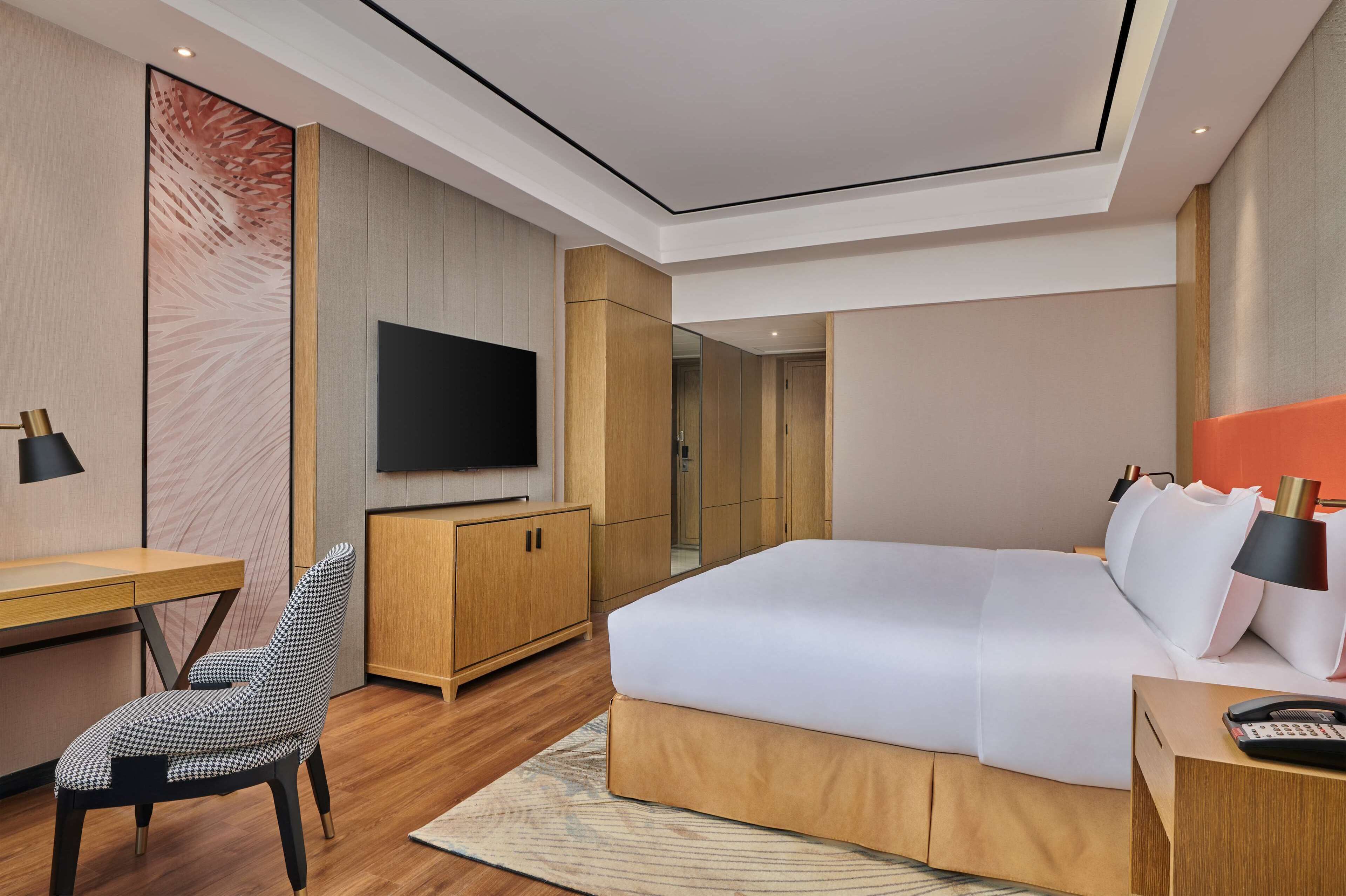 Una habitación de hotel moderna con una cama grande, un escritorio, una silla, un televisor y un armario.