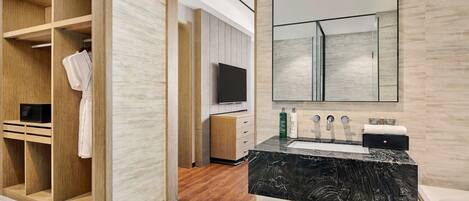 Un baño moderno con un lavamanos de mármol, un espejo grande y un vestidor con estantes de madera.