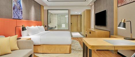 Una habitación de hotel moderna con una cama grande, un escritorio, un televisor y un baño visible a través de una puerta abierta.