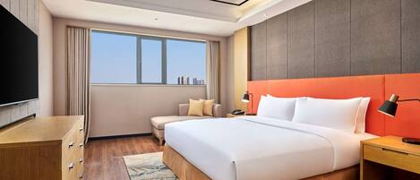 A modern hotel room with a large bed, a desk, a TV, and a city view.