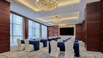 Un salón de conferencias con filas de mesas y sillas, ventanas amplias y candelabros.