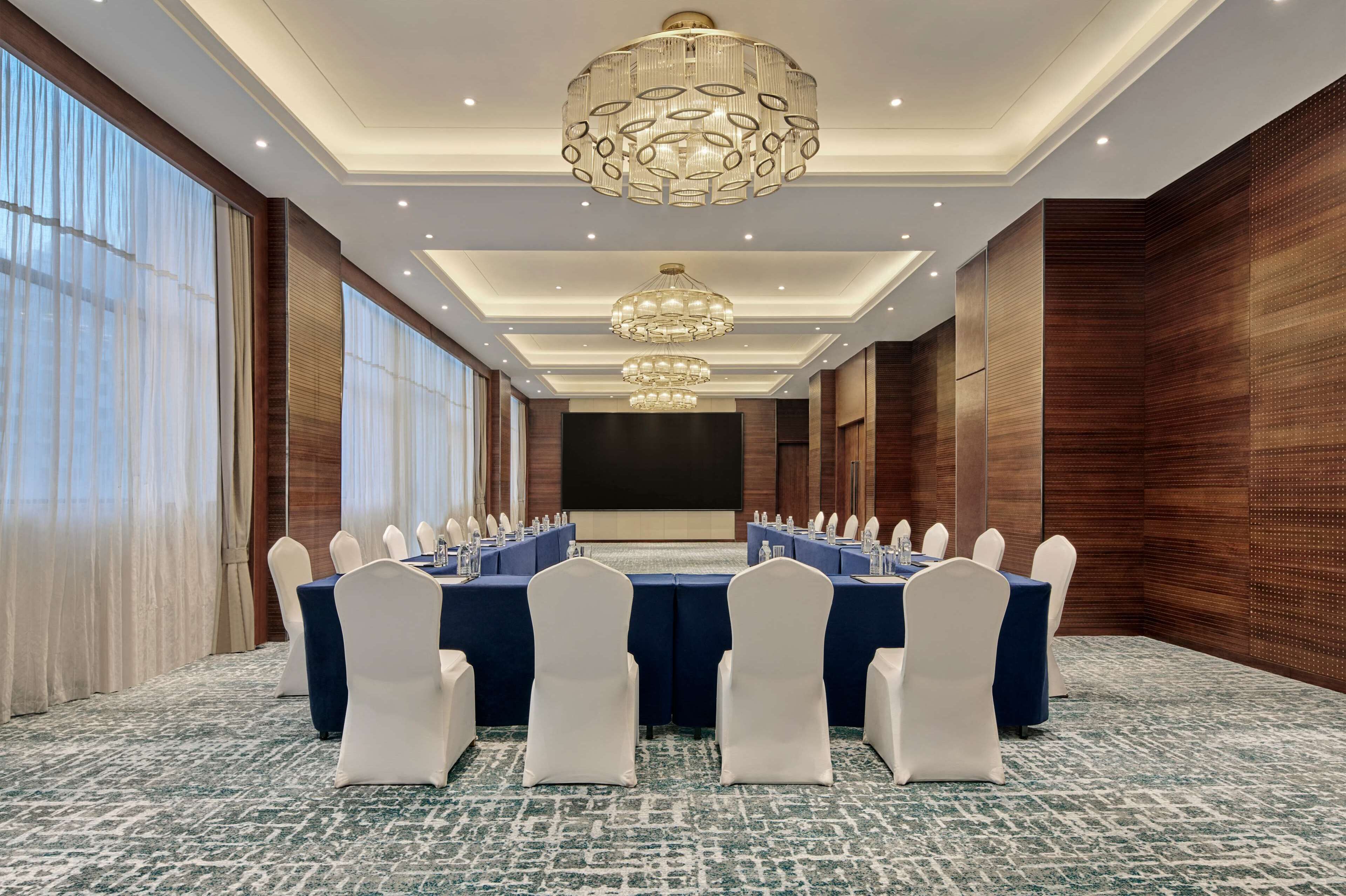 A conference room with a long table, white chairs, and a large chandelier.