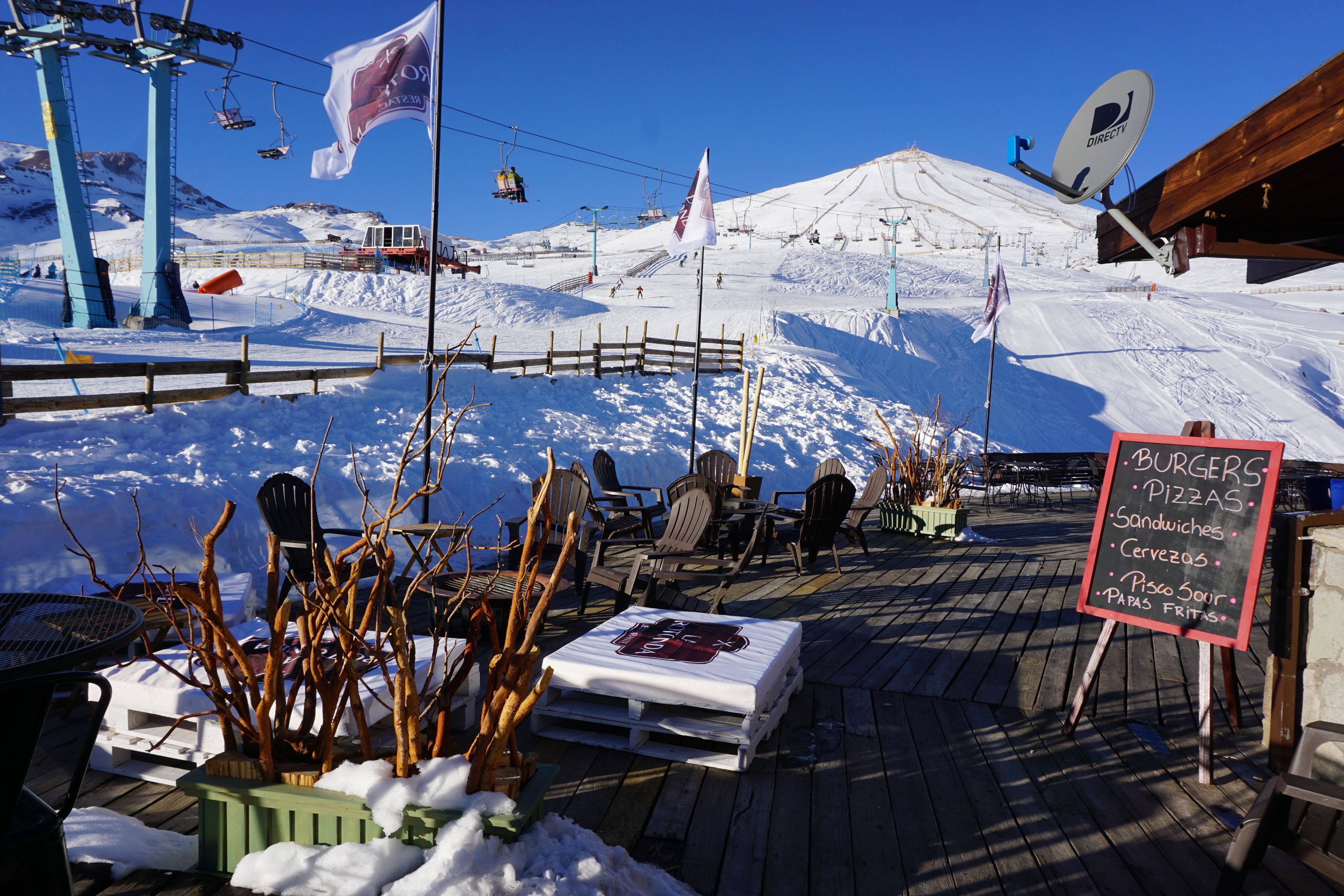 A snow-covered outdoor seating area with a menu board listing burgers, pizzas, sandwiches, and other items.