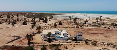 A desert resort with a pool, palm trees, and a view of the ocean.