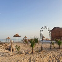 A beach with a wooden hut, thatched umbrellas, and a metal archway.