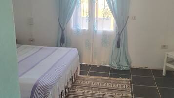 A bedroom with a bed, a patterned rug, and a window with curtains.