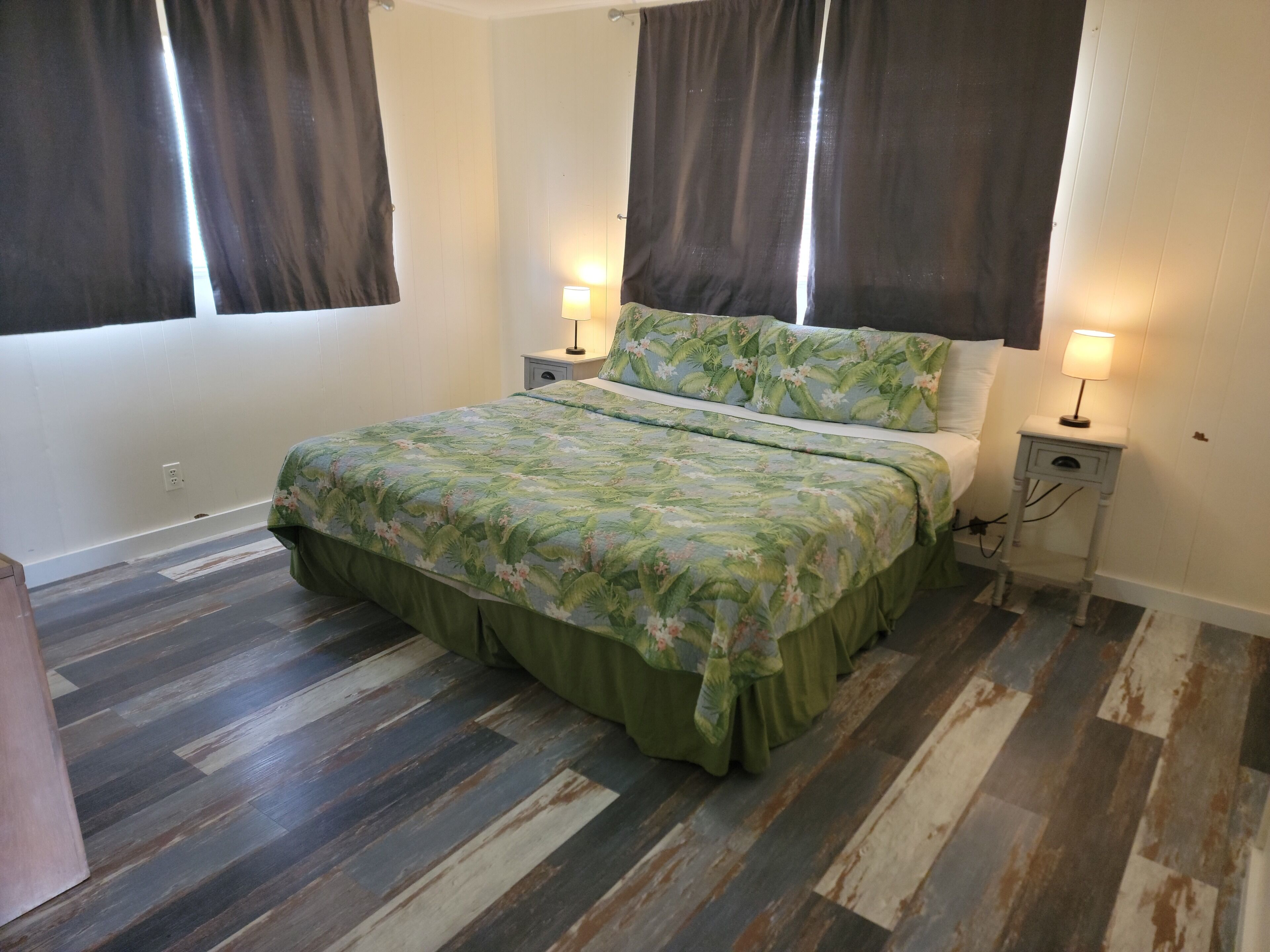 A bedroom with a bed, two bedside tables, a nightstand, and a window with curtains.