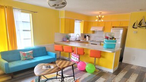 A compact living space with a blue sofa, a small round table, and a kitchen area featuring yellow cabinets and a white refrigerator. - Upper Deck Hotel and Bar - Adults Only (South Padre Island)