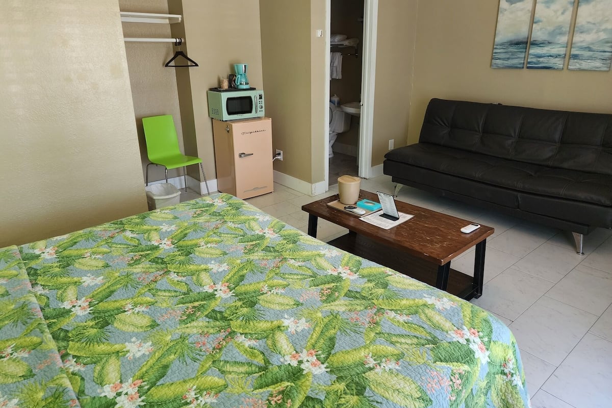 A room with a bed, a couch, a small kitchenette, and a bathroom visible through an open door.
