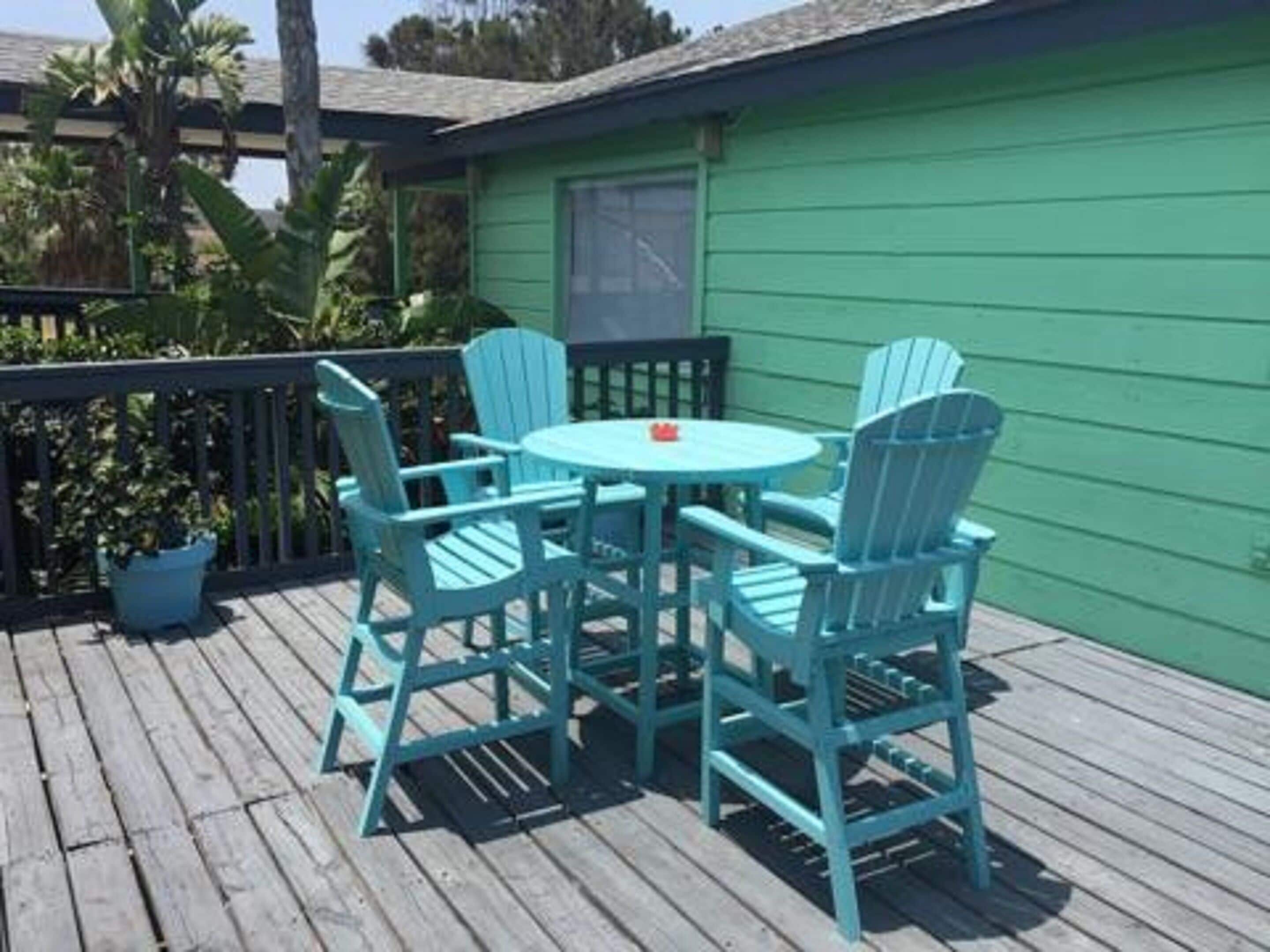 A green house with a wooden deck, a round table, and four matching chairs.