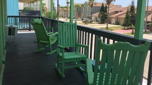 A covered porch with green Adirondack chairs and a view of residential buildings and palm trees. - Upper Deck Hotel and Bar - Adults Only (South Padre Island)