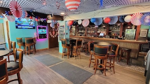 A bar area with wooden tables and chairs, a neon sign, and various decorations including paper fans and a 'No ID Required' sign. - Upper Deck Hotel and Bar - Adults Only (South Padre Island)