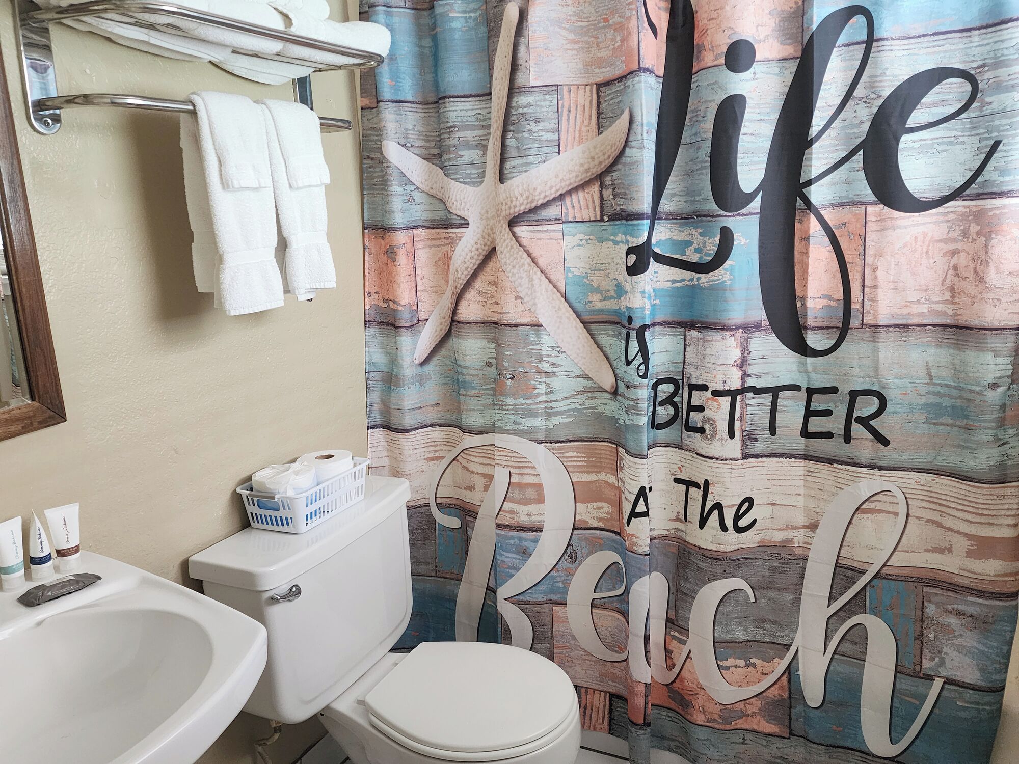 Une salle de bain avec un rideau de douche orné d’une étoile de mer et de l’inscription : « La vie est plus belle à la plage. »