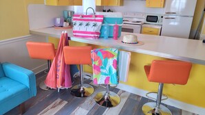 A kitchen with yellow cabinets, a white refrigerator, and a bar area with orange stools. - Upper Deck Hotel and Bar - Adults Only (South Padre Island)