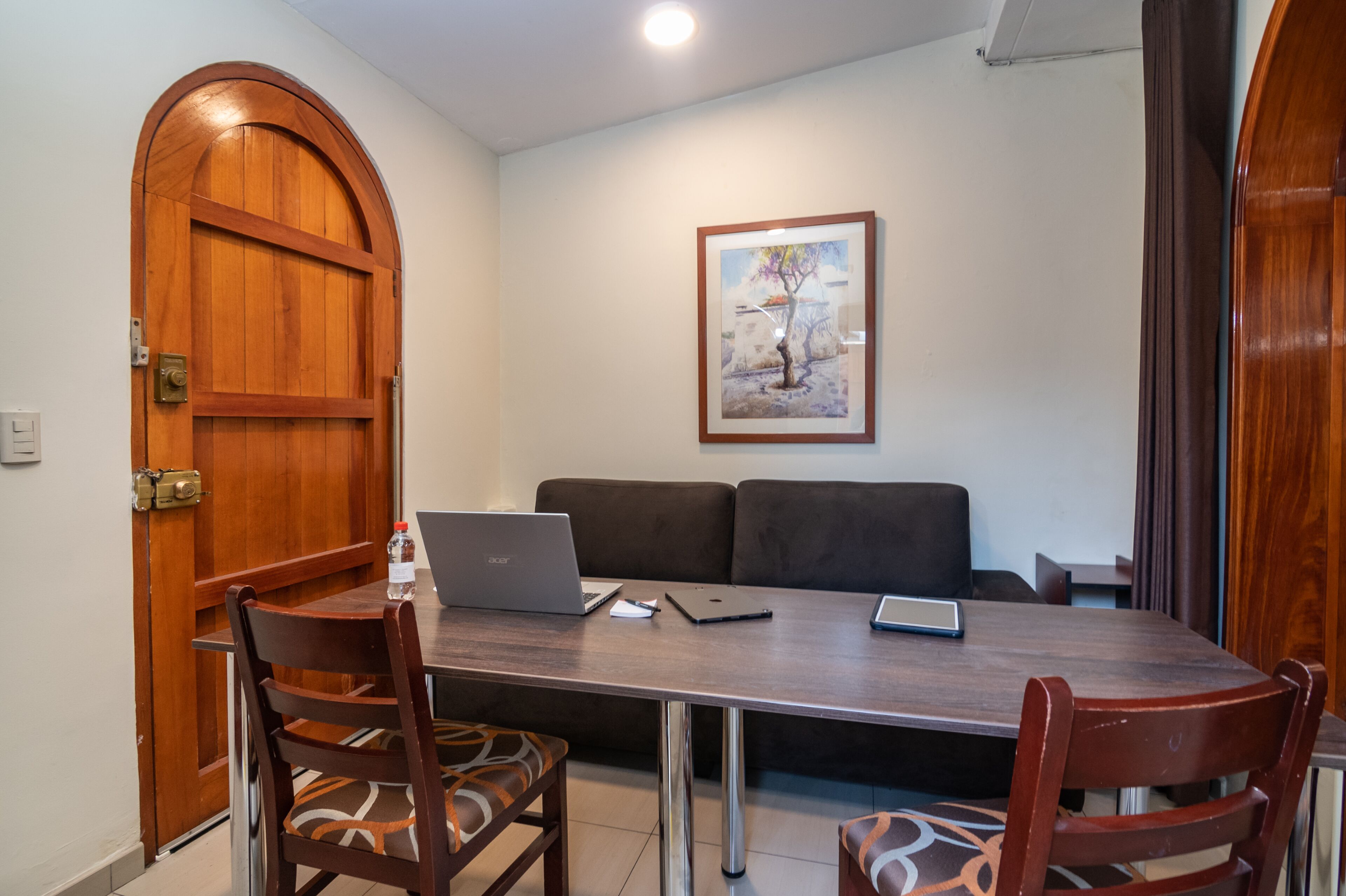 Un comedor con una mesa de madera, sillas, una computadora portátil y un cuadro en la pared.