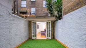 A narrow courtyard with artificial green turf, white brick walls, and a wooden deck. - Marylebone Apartments (London)
