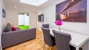 A modern living room with a sofa, dining table, chairs, and a large cityscape painting. - Marylebone Apartments (London)