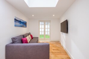 A modern living room with a grey sofa, a flat-screen TV, and a painting of a mountain landscape. - Marylebone Apartments (London)