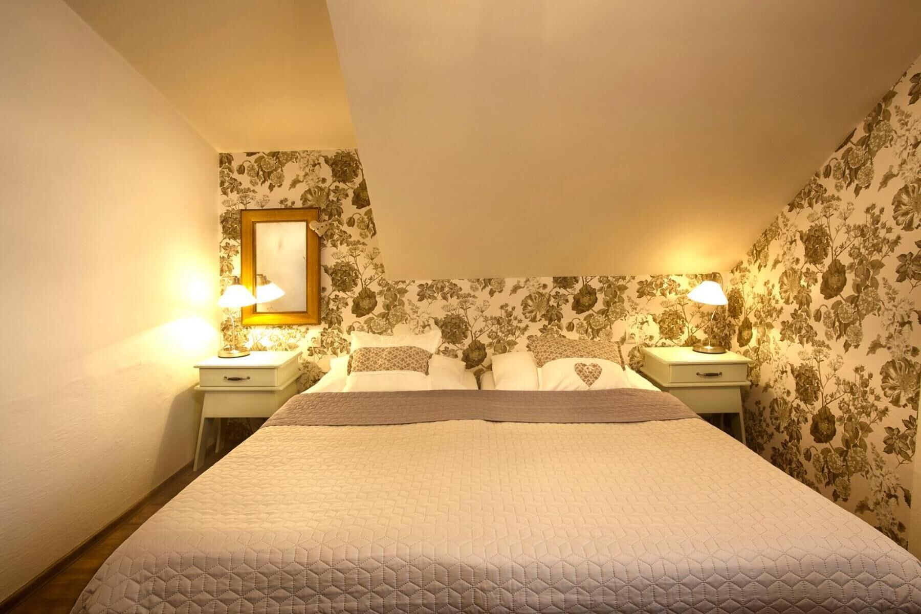 A hotel room with a bed, two bedside tables, a nightstand, a lamp, and floral wallpaper.