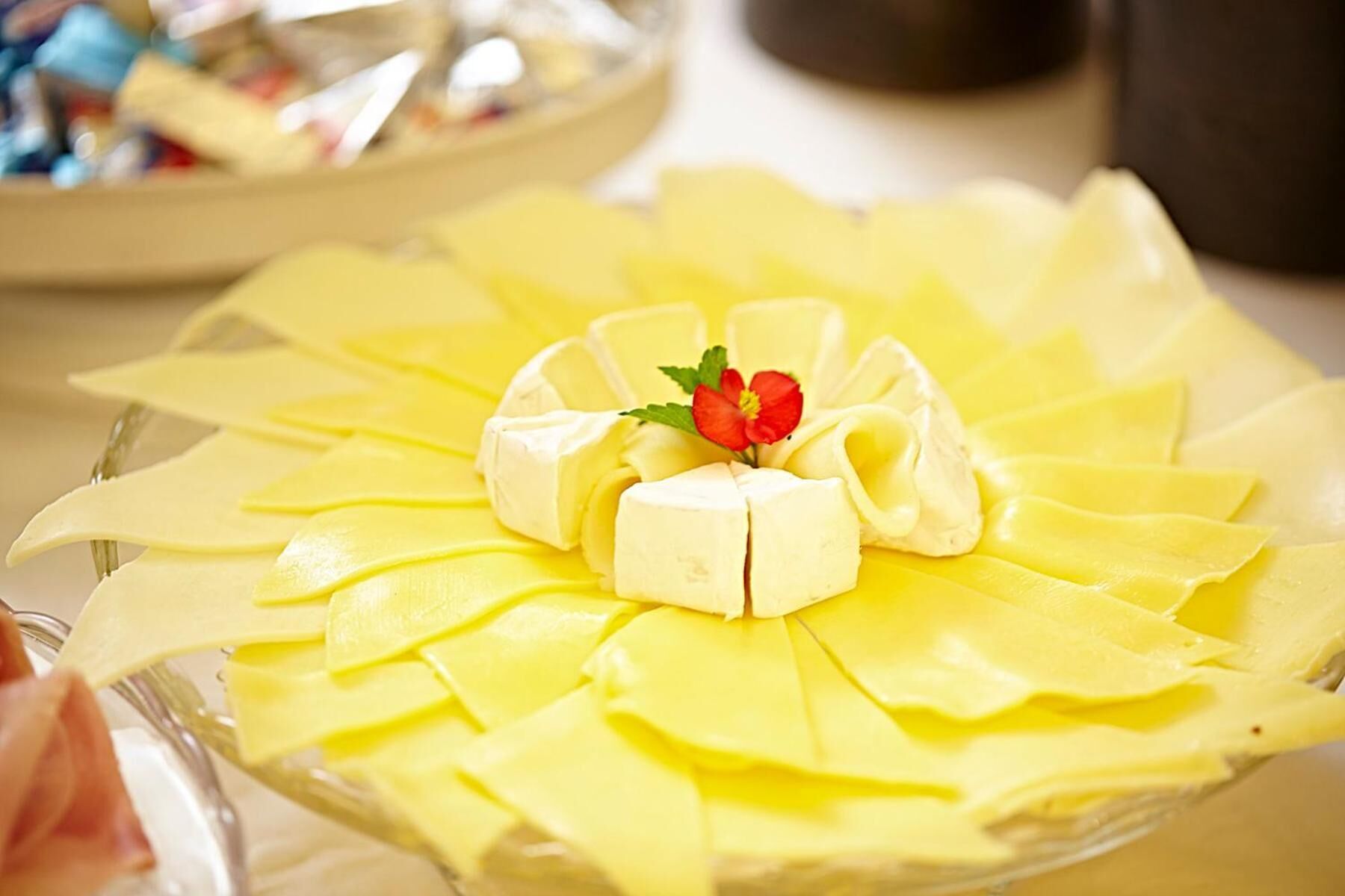 Un plato de postres con porciones de pastel amarillo dispuestas en forma circular, coronado con una cucharada de crema y una pequeña flor roja.