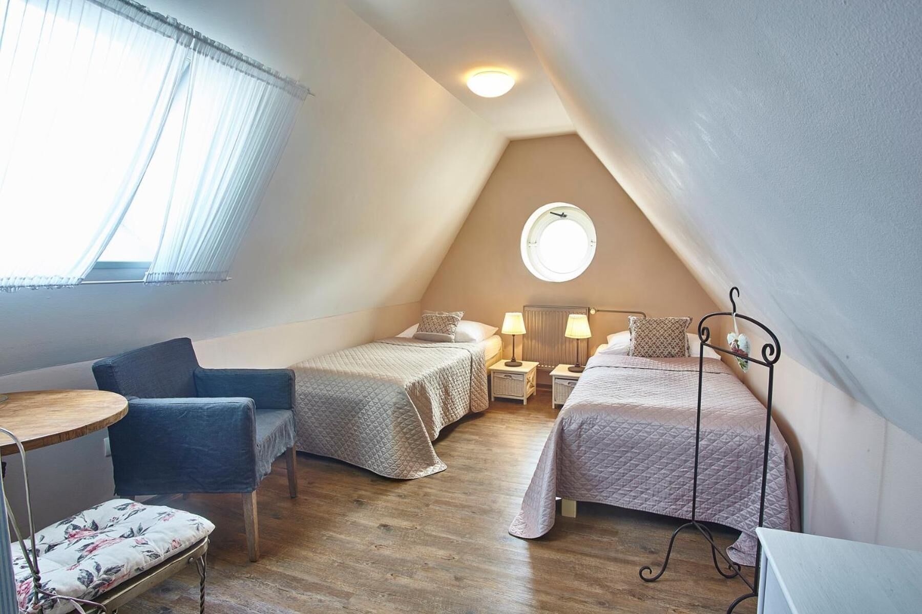 A cozy attic bedroom with two beds, a small table, and a chair.