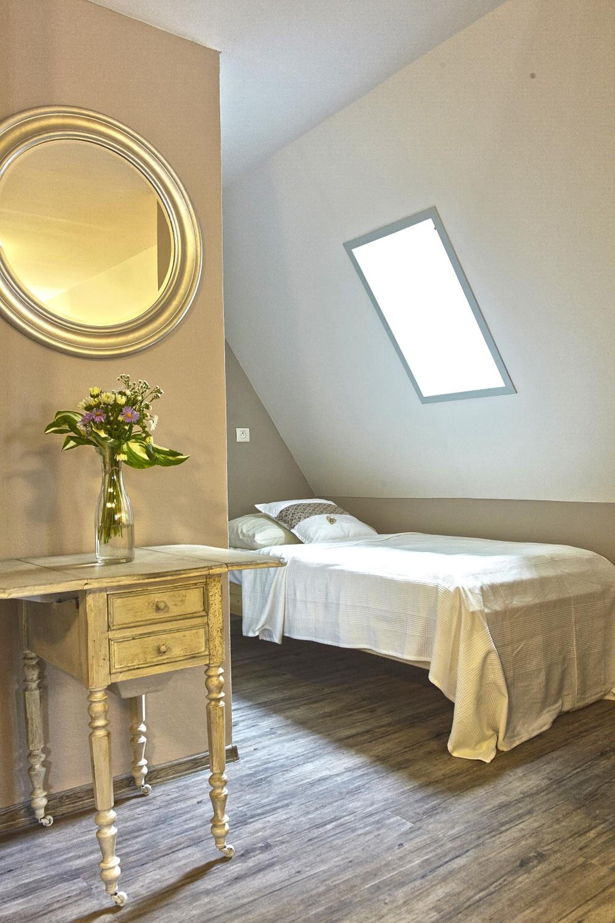 Une chambre à coucher avec un lit, une commode, un miroir et une lucarne.