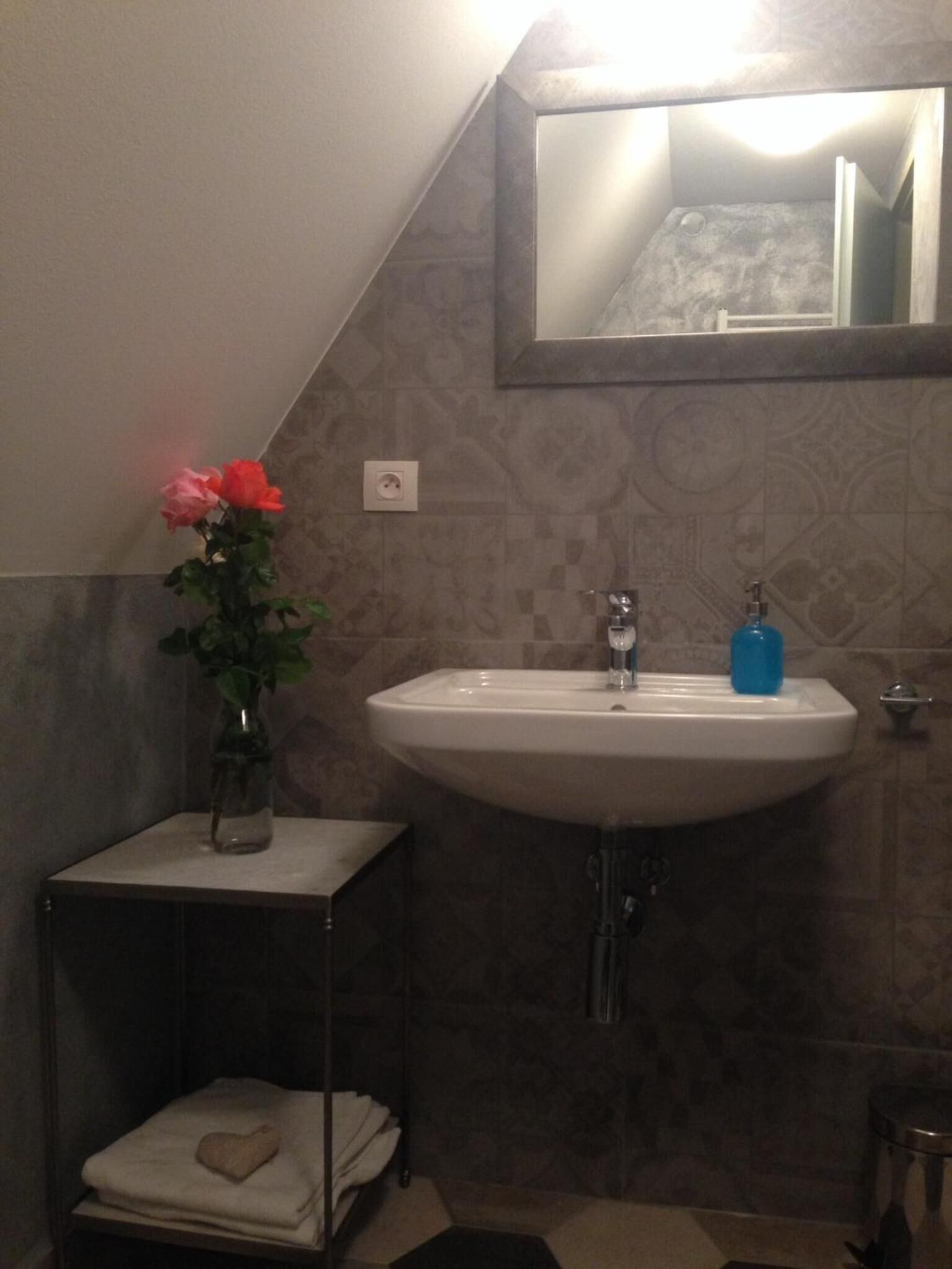 A bathroom with a sink, a mirror, and a vase with flowers.
