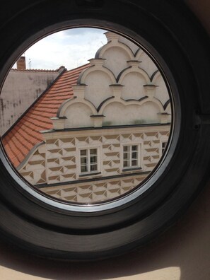 Una ventana con vistas a un edificio que presenta una fachada con diseños y un tejado de tejas rojas.