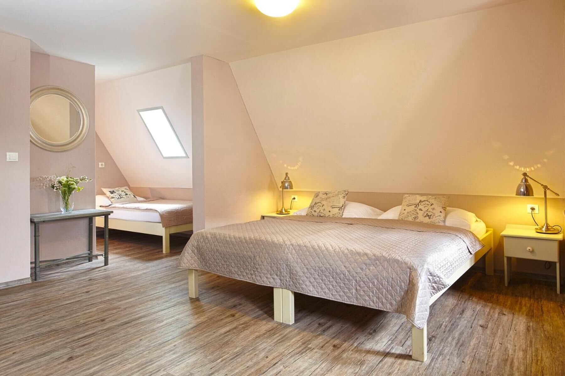 A bedroom with a bed, bedside tables, a mirror, and a skylight.