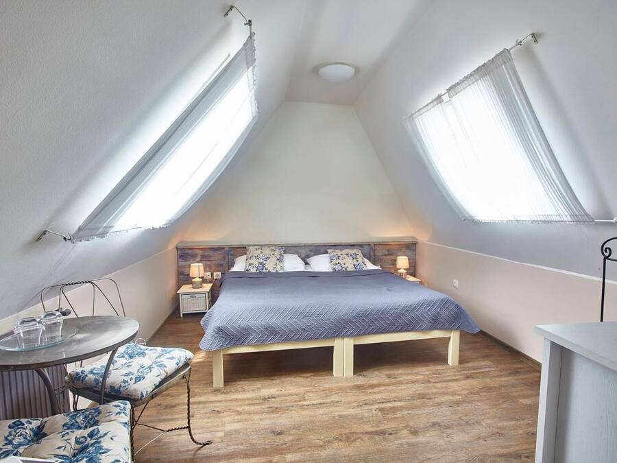 A small, cozy bedroom with a bed, bedside tables, and a chair.