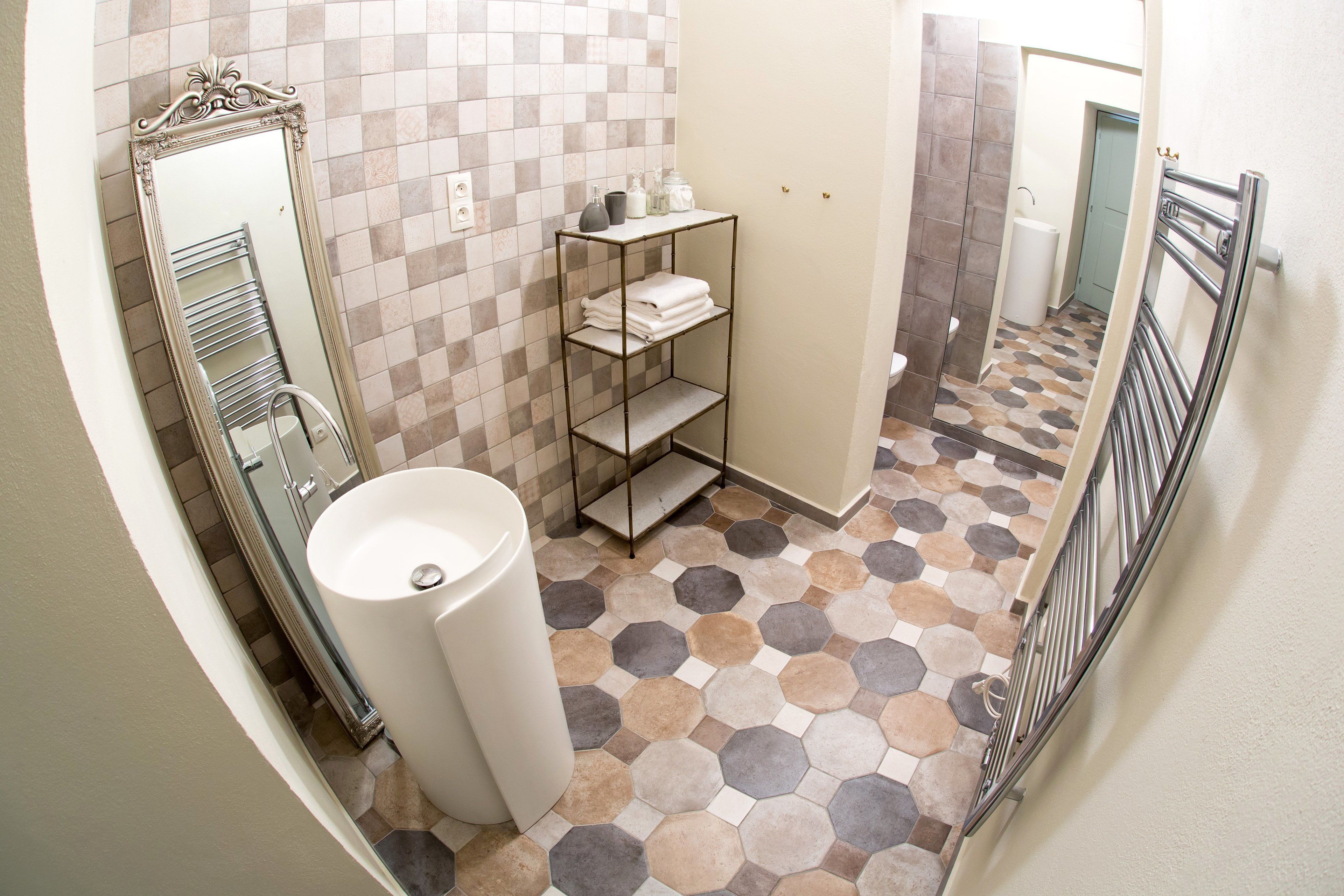 A bathroom with a tiled floor, a white sink, a mirror, and a metal shelf with towels.