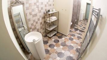 A bathroom with a tiled floor, a white sink, a mirror, and a metal shelf with towels.