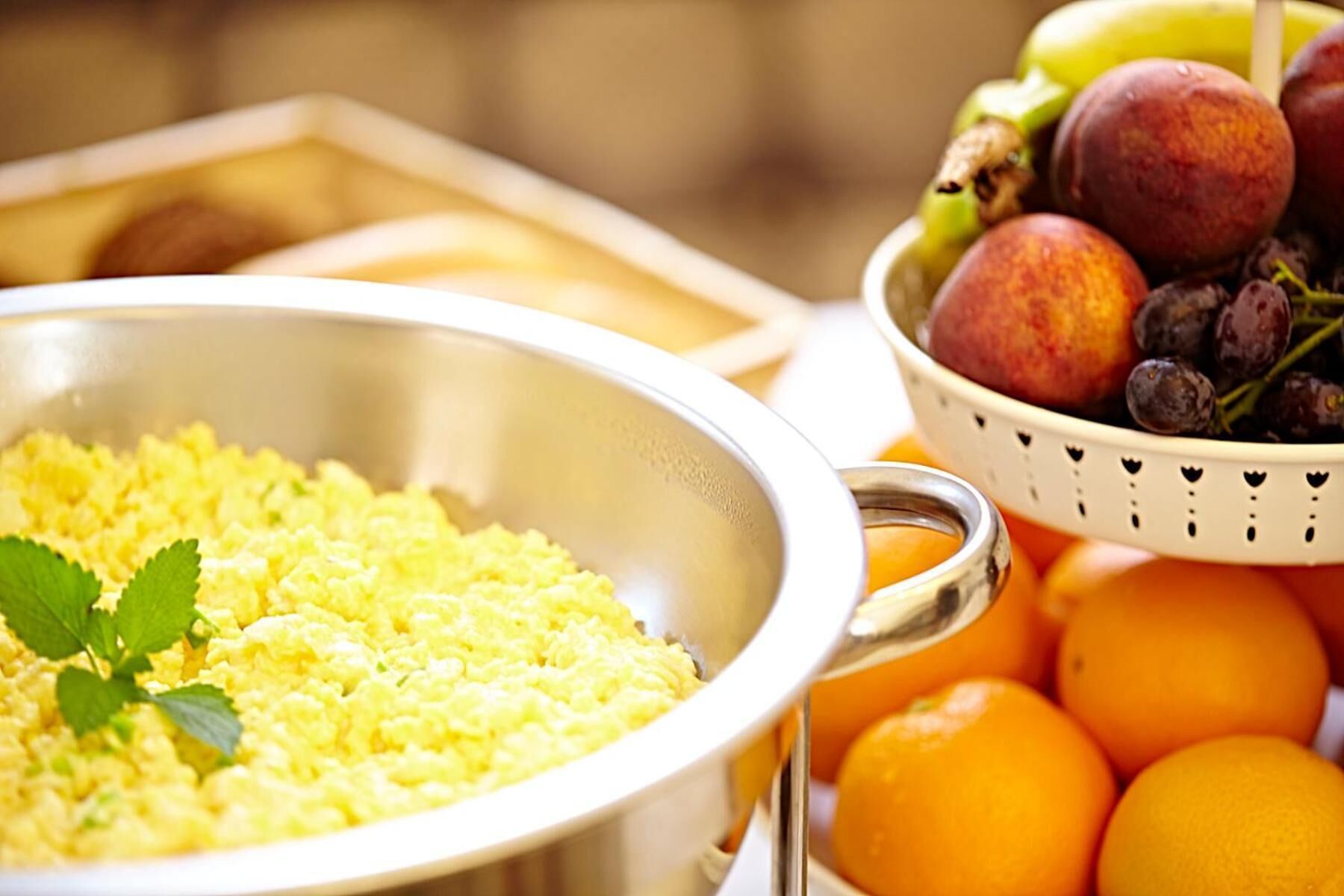Een ontbijttafel met roerei, een fruitschaal en sinaasappels.