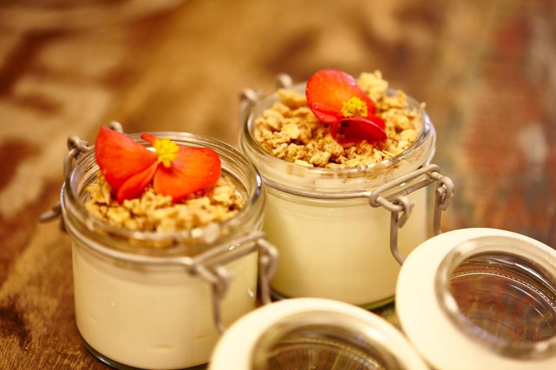 Drei Dessertgläser mit Blüten-Garnitur auf einer Holztischplatte.