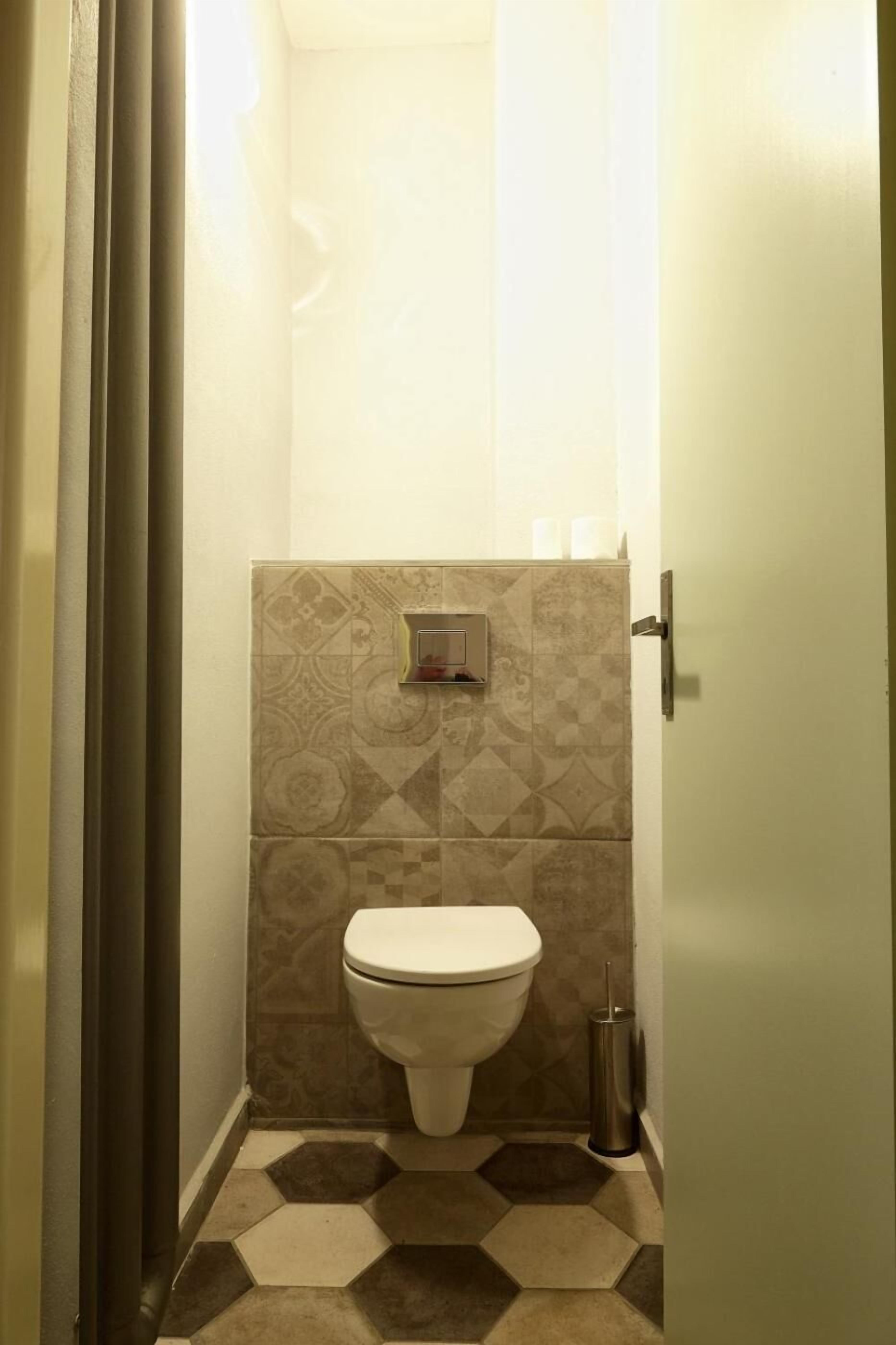 Un baño pequeño y estrecho con inodoro, secamanos y cubo de basura.