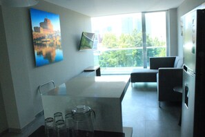 A modern kitchen with a glass dining table, a coffee maker, and a large window offering a city view.