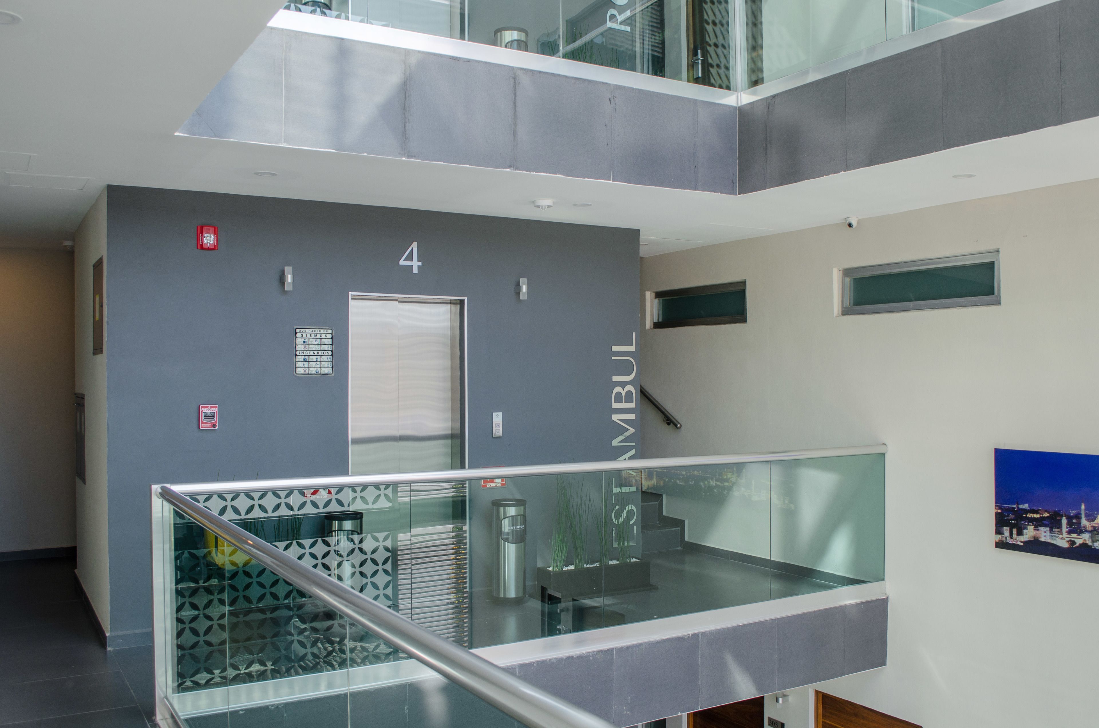 Un interior moderno con barandilla de vidrio, una puerta con el número 4 y una escalera.