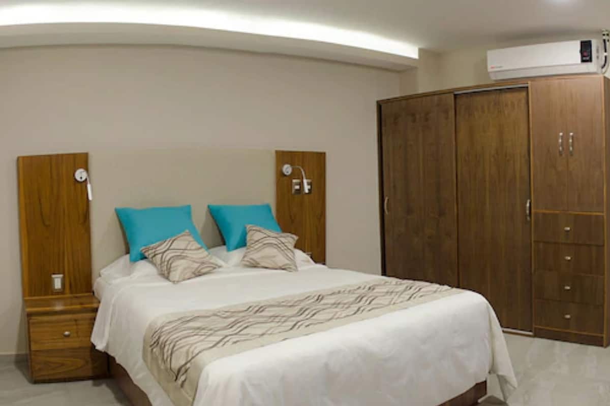 A bedroom with a bed, two nightstands, a wardrobe, and an air conditioning unit.
