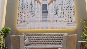 Un'ampia hall con zona salotto centrale, soffitto alto e design simmetrico con colonne e lampadari.