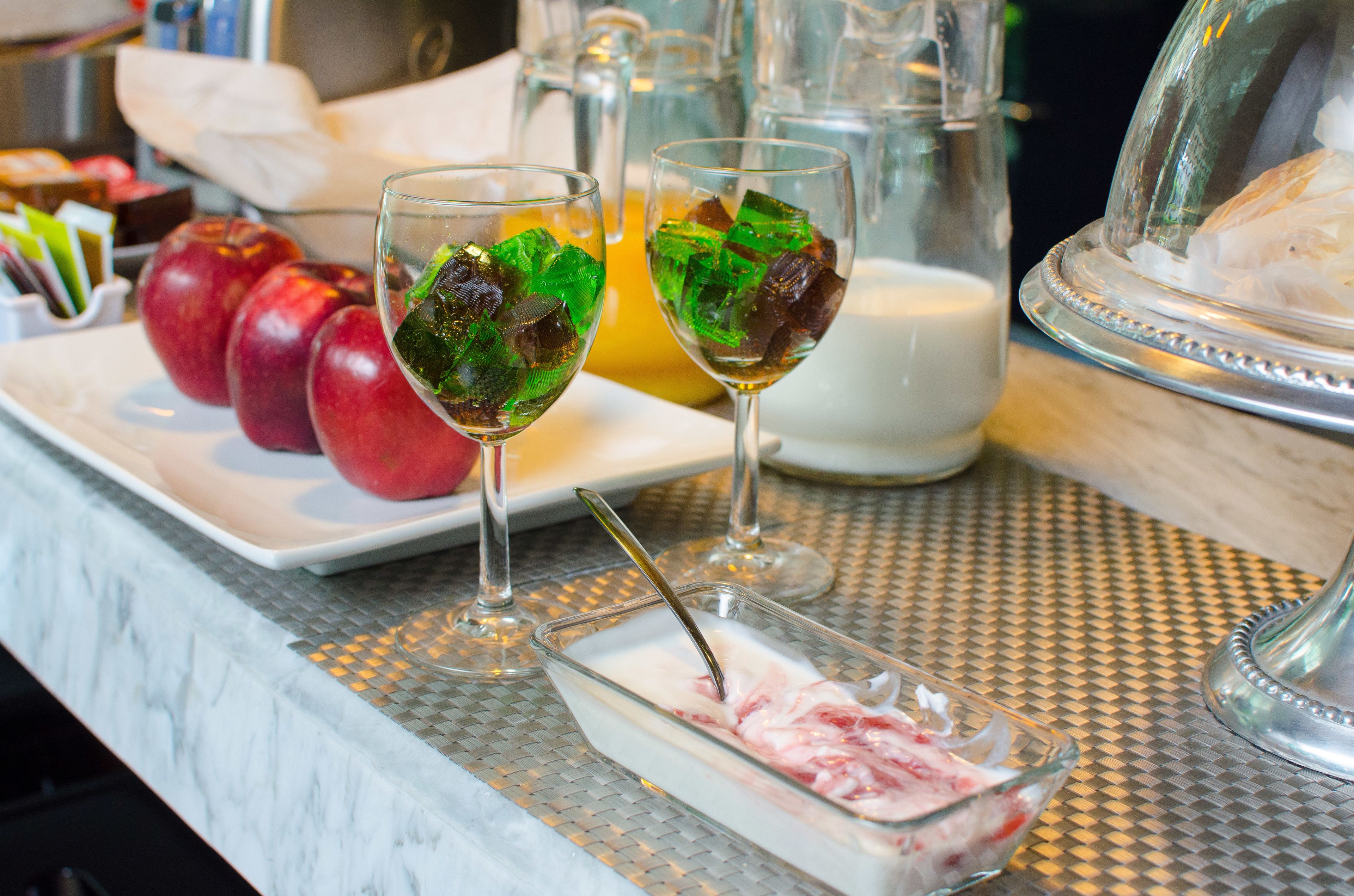 A breakfast setting with a plate of red apples, two glasses with green ice cubes, a glass of orange juice, and a glass of milk.
