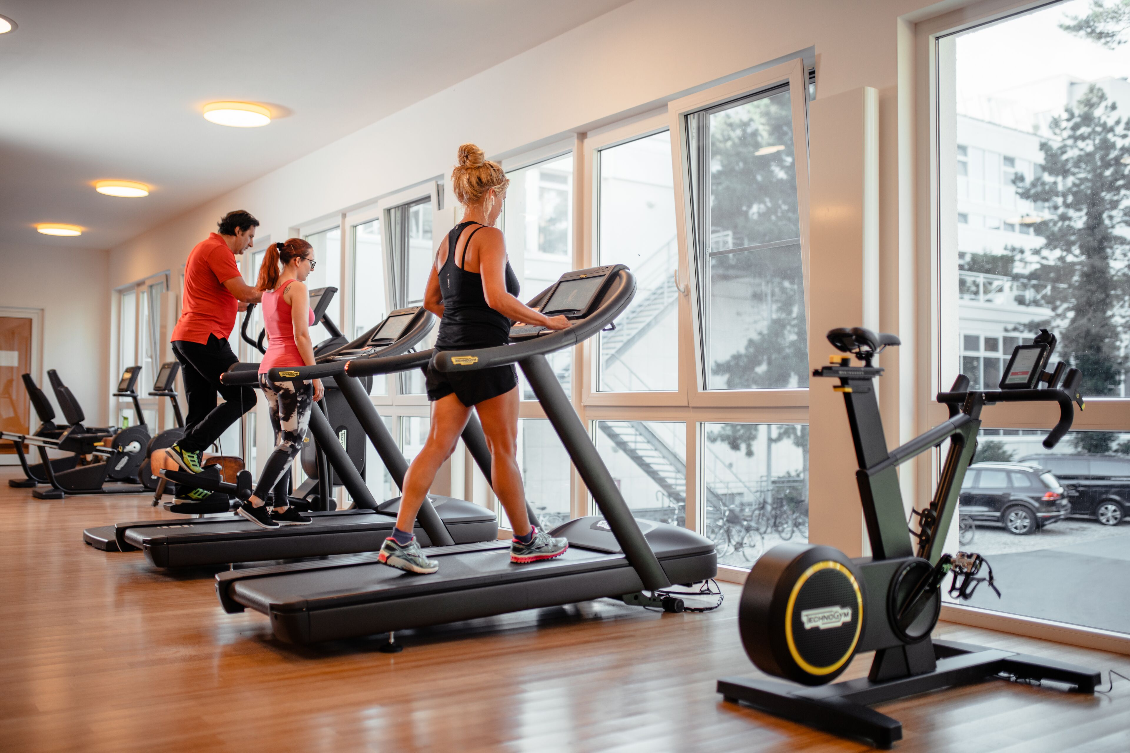 Een sportschool met loopbanden, hometrainers en grote ramen.