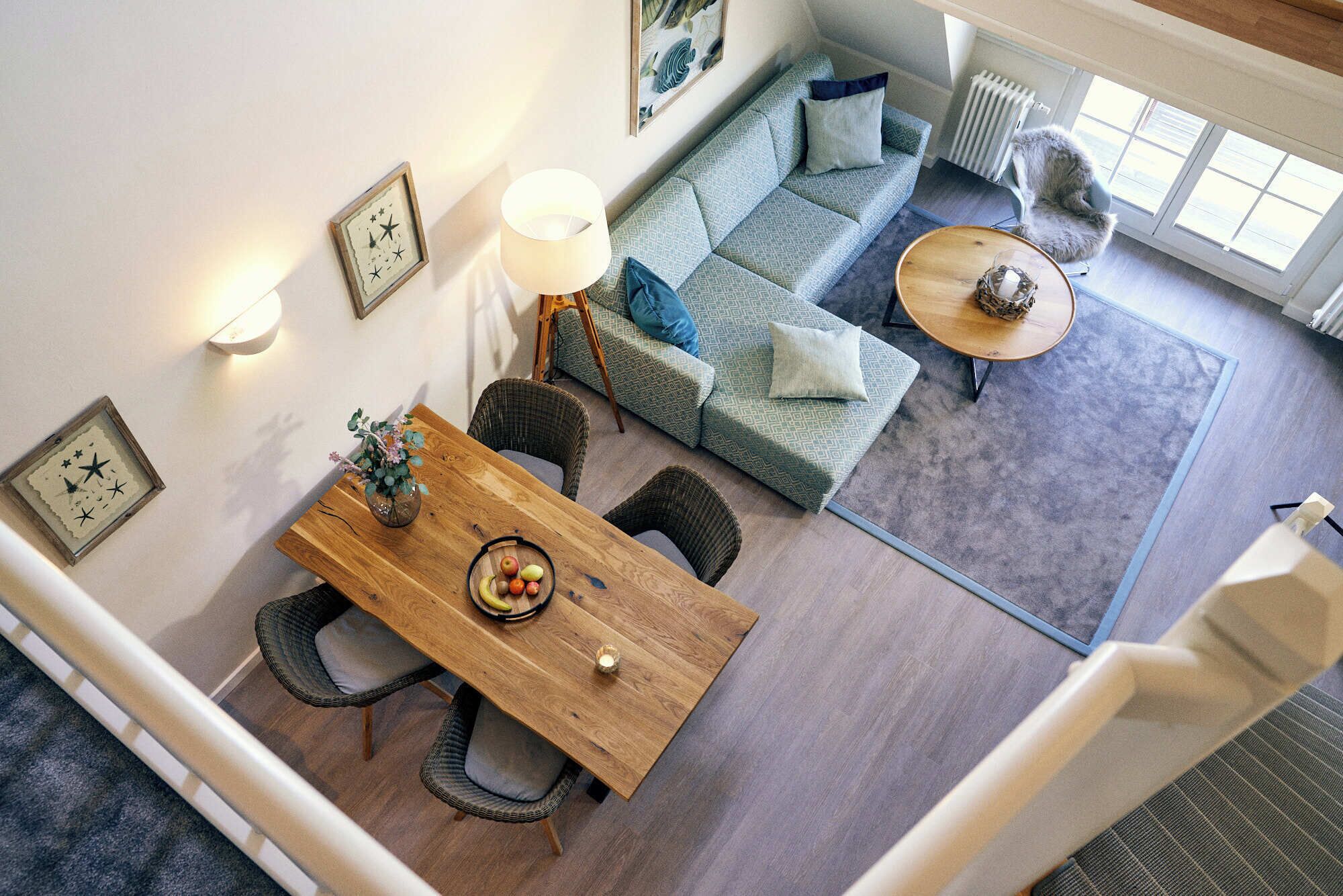 Una sala de estar moderna con una mesa de comedor de madera, sillas de mimbre, un sofá azul con estampado y una mesa de centro redonda.