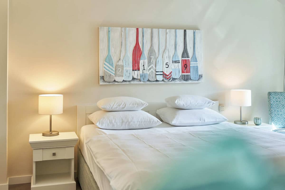 A hotel room with a bed, two bedside tables with lamps, a wall-mounted painting, and a patterned cushion.