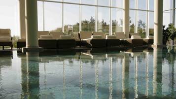 An indoor swimming pool with clear water, large windows, and lounge chairs.